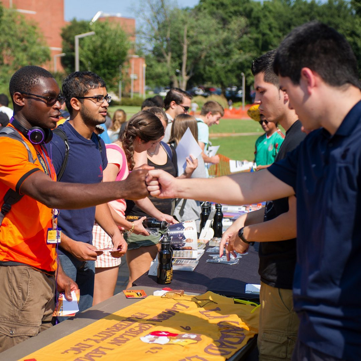 Women and men students during the RSOs outside fair. Two men fist bump.
